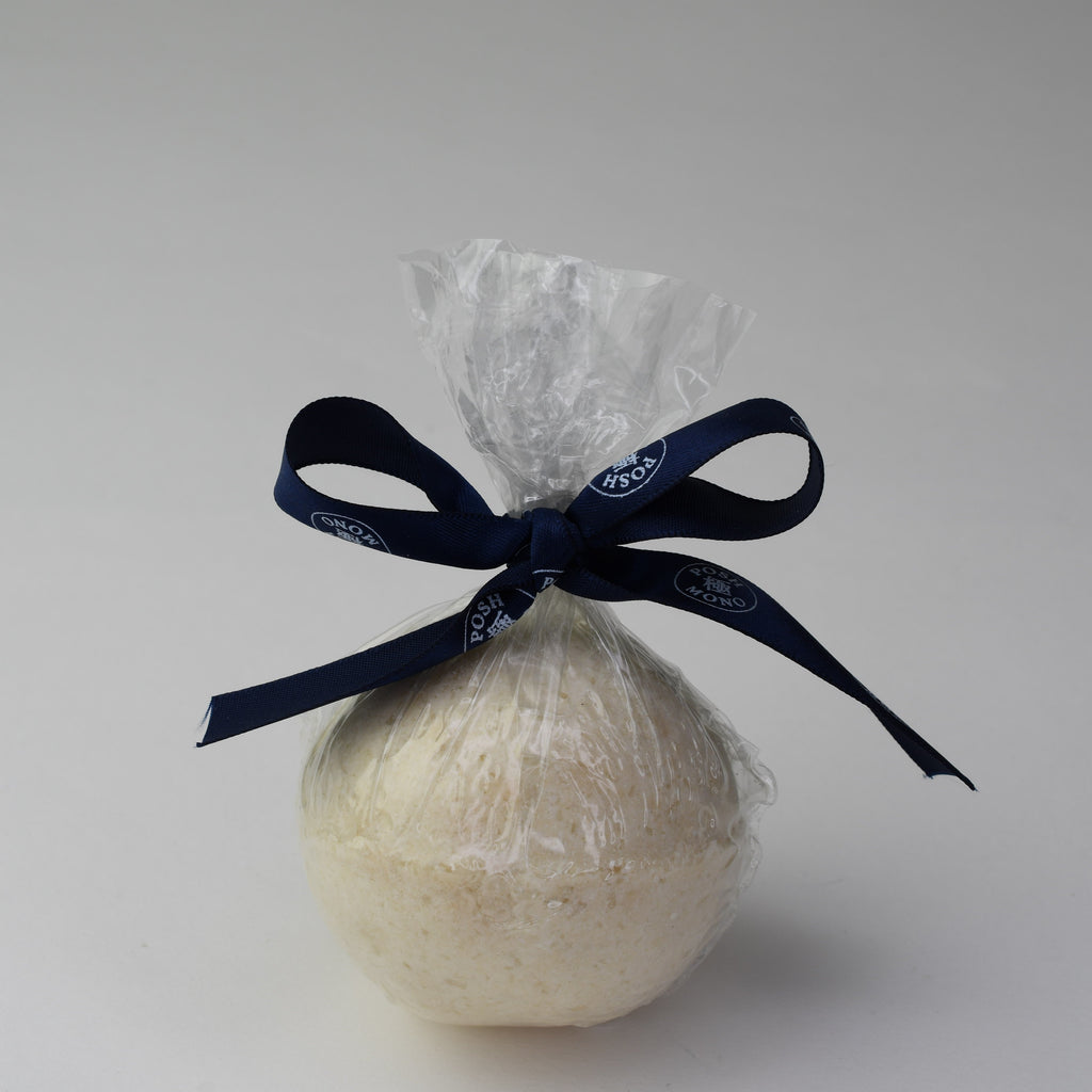 Bath bomb wrapped in cellophane with a blue ribbon on a light gray background