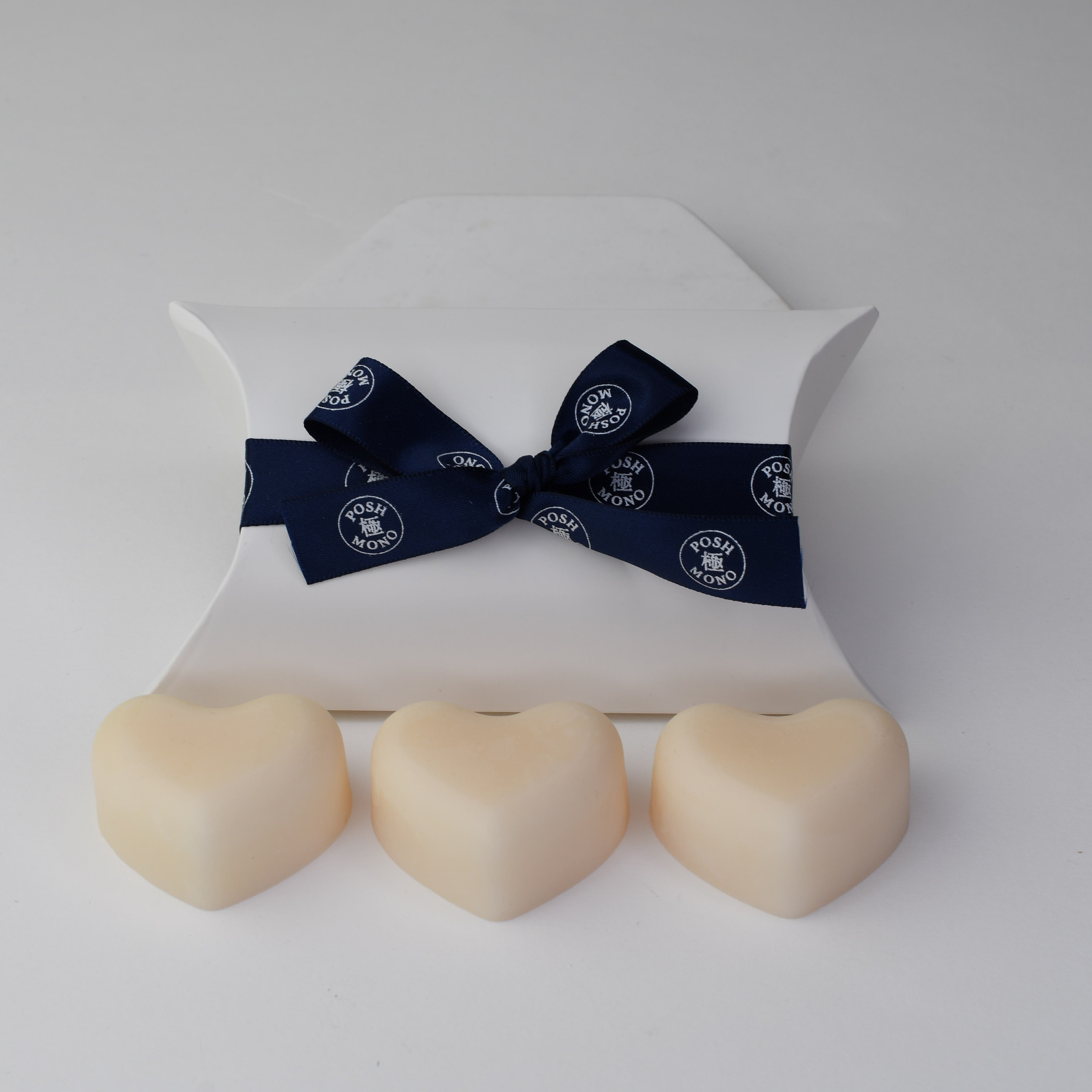 Three heart-shaped wax melts in a white box with a navy ribbon on a light gray background